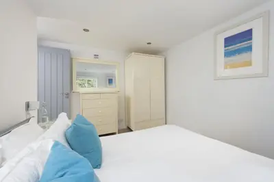 a white bedroom with a large bed with blue pillows at Salubrious Cottage, St Ives in St Ives