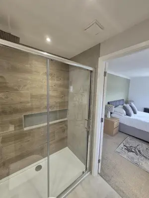 a glass shower in a bedroom with a bed at Whispering Waters in Newquay