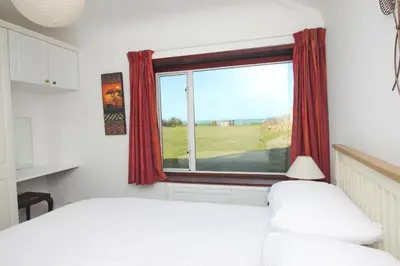 a bedroom with a bed and a window with red curtains at ON THE BEACH holiday home in St Merryn