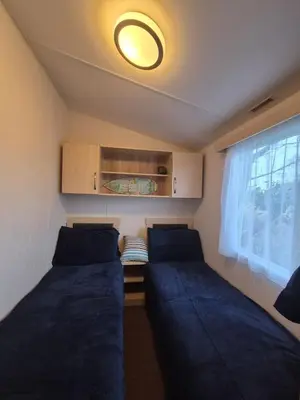 a small room with two beds and a window at Cosy Perranporth caravan, Cornwall in Perranzabuloe