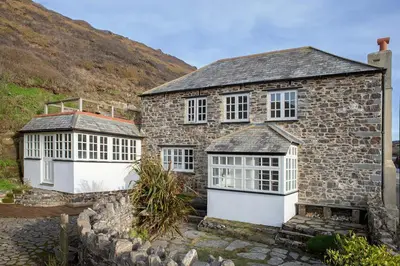 a stone house with white windows and a stone wall at Penkenna House - magical home and location Saturday to Saturday bookings only 7 night min July to October in Crackington Haven