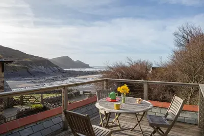 a table and chairs on a balcony with a view of the beach at Penkenna House - magical home and location Saturday to Saturday bookings only 7 night min July to October in Crackington Haven