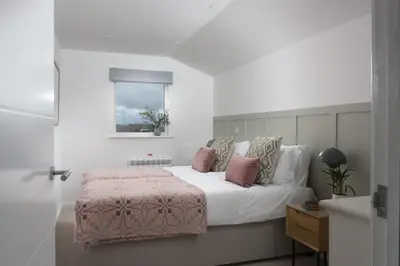 a bedroom with a bed with white sheets and pink pillows at Carbis Bay Lodge - Spa Facilities & Woodburner in Carbis Bay