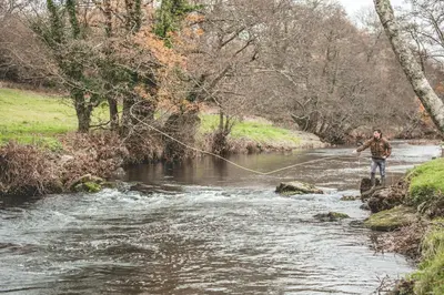 a man is standing in a river while holding a fishing line at Riverside farm cottage on private wildlife estate 1-bedroom in Washaway