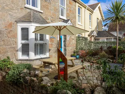 a wooden picnic table with an umbrella in front of a house at The Haven in Marazion