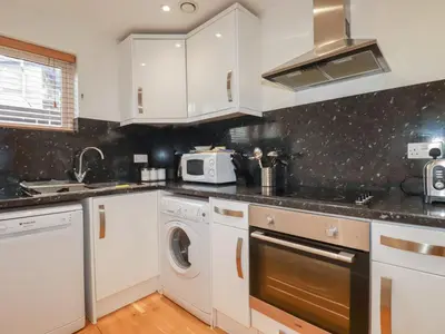 a kitchen with white cabinets and a washer and dryer at Treveglos in Truro