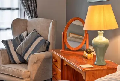 a chair and a lamp on a table with a mirror at Finest Retreats - Orchard View in Hayle