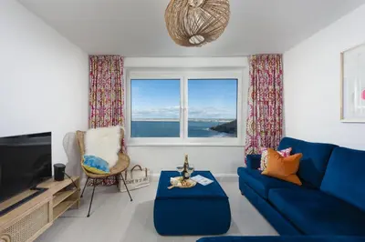 a living room with a blue couch and a window at Pink Sands, Carrack Widden, St Ives in St Ives