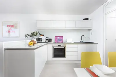 a white kitchen with white cabinets and yellow chairs at Pink Sands, Carrack Widden, St Ives in St Ives