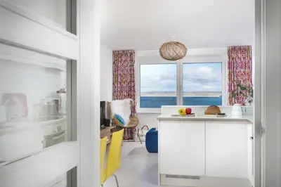 a kitchen with white cabinets and two windows at Pink Sands, Carrack Widden, St Ives in St Ives