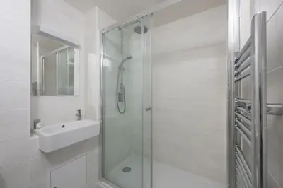a white bathroom with a shower and a sink at Pink Sands, Carrack Widden, St Ives in St Ives