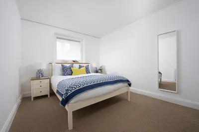 a white bedroom with a bed and a mirror at Pink Sands, Carrack Widden, St Ives in St Ives