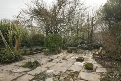 a garden with a stone patio with benches and trees at Homely Cottage & Garden nr Praa Sands & Marazion in Saint Hilary