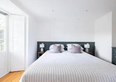 a white bedroom with a large bed with purple pillows at First-Floor Georgian Apartment with Terrace and Sea Views in Boscastle in Boscastle
