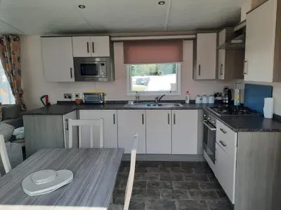 a kitchen with white cabinets and a table in it at Luxury 6 berth caravan full decking in Saint Columb Minor