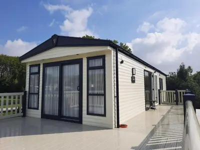 a small white building with windows on a deck at Luxury 6 berth caravan full decking in Saint Columb Minor