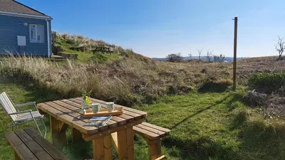 a wooden picnic table in the grass next to a house at G17 St Meva, Riviere Towans in Hayle