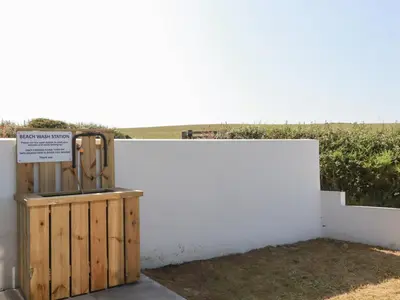 a white wall with a wooden box next to a field at Jacana in Perranporth