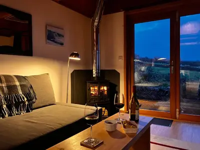 a living room with a fireplace and a couch with wine glasses at Seaview Studio in Forrabury