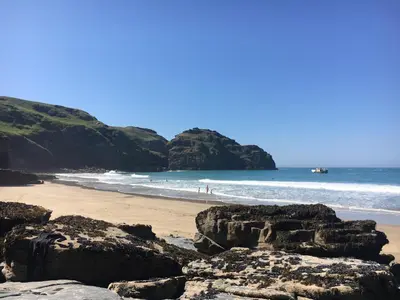 a beach with rocks and the ocean with people in the water at Seaview Studio in Forrabury