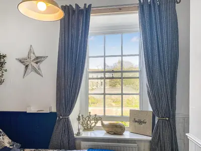 a bedroom with blue curtains and a window at Issys Cottage in Helston