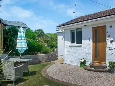 a small white house with an umbrella and a table at Chlobo Cottage in Porth