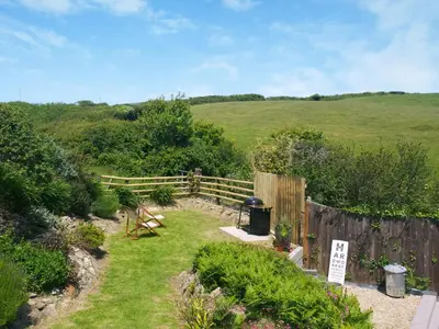 a garden with a wooden fence and a hill in the background at Chlobo Cottage in Porth