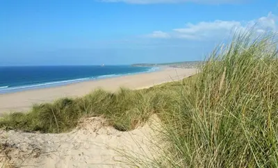 a sandy beach with some grass and the ocean at Family Home in Hayle close to Gwithian Beach in Phillack