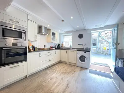 a kitchen with white cabinets and a washer and dryer at Howards Way in St Ives