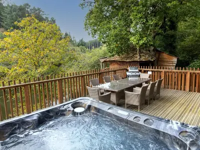 a hot tub on a deck with a table and chairs at Deerpark Cabins, Cornwall - Forest Holidays in Liskeard