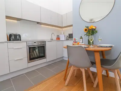 a kitchen with white cabinets and a wooden table and chairs at Azure Retreat at Una in St Ives
