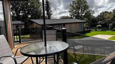a glass table and two chairs on a balcony at Manor Lake Lodge Exclusive luxury lodge retreat in Saint Tudy