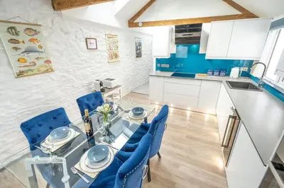 a dining room with a glass table and blue chairs at Beautiful Quayside Cottage Looe in Looe