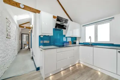 a kitchen with white cabinets and blue accents at Beautiful Quayside Cottage Looe in Looe