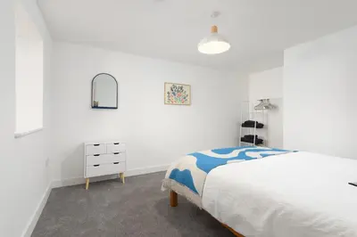a white bedroom with a bed and a dresser at Hednes Barn in Crowan