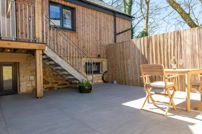 a patio with a table and a chair and a building at Hednes Barn in Crowan