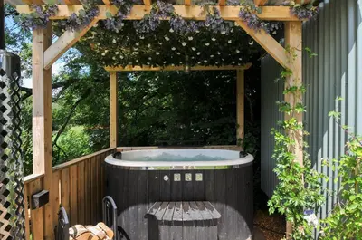 an outdoor hot tub in a pergola with a bench at The Highwood Hut in Liskeard