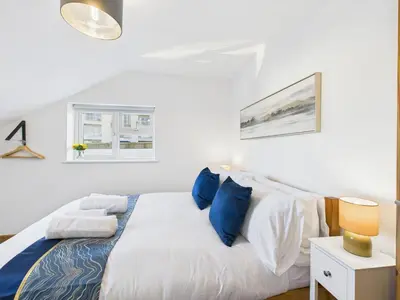 a white bedroom with a bed with blue pillows at Surf View by Signature Stays - Pool - Beach Access in Crantock