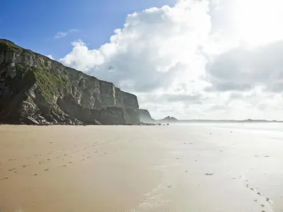 a beach with footprints in the sand next to a cliff at Tide & Treth in Newquay