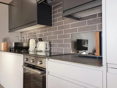 a kitchen with white cabinets and a brick wall at Priory in St Austell