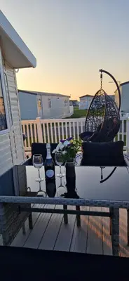 a table with wine glasses and a basket on a deck at HolidayLet 24 Bude Newperran Holiday Park in Cubert