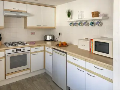 a kitchen with white cabinets and white appliances at Chy An Mordros in Hayle