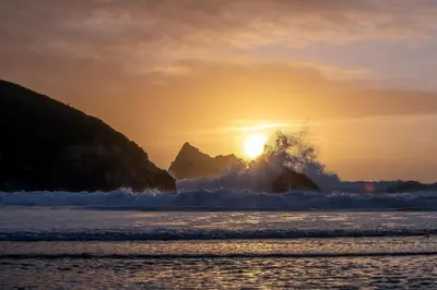 a sunset over the ocean with a wave crashing on the rocks at 14 Azure in Fistral, Newquay in Newquay