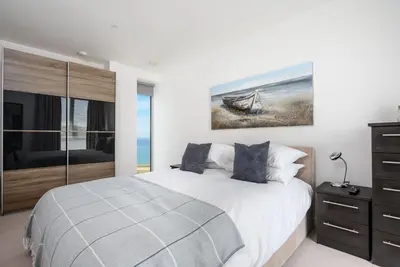 a white bedroom with a bed and a painting on the wall at 32 One Lusty Glaze in Newquay in Newquay