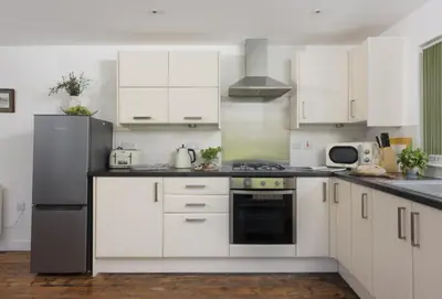 a kitchen with white cabinets and a black refrigerator at Ivy Chimney Cottage near Scorrier and close to Porthtowan in Porthtowan
