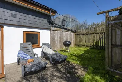 a patio with two chairs and a grill in a yard at Ivy Chimney Cottage near Scorrier and close to Porthtowan in Porthtowan