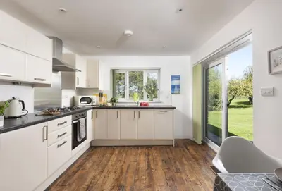 a kitchen with white cabinets and a large window at Ivy Chimney Cottage near Scorrier and close to Porthtowan in Porthtowan