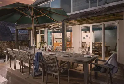 a wooden table with chairs and a green umbrella at Gull Rock in Padstow