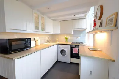 a kitchen with white cabinets and a washer and dryer at 4 Victoria House with the best views in St Ives in St Ives