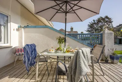a table and chairs with an umbrella on a deck at Bluebirds in Polzeath